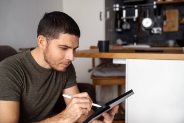 Kanepede oturan bir adam internette haber ya da çizim aramak için tablet ve kalem kullanıyor. Uzak ev işleri.