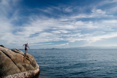 Tayland 20 Mart 2017: Taştan bir sahilde yetişkin bir balıkçı deniz manzarasının arka planında bir balık yakalar..