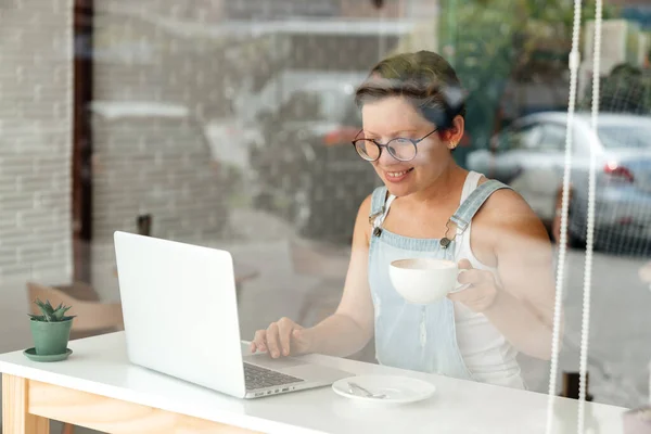 Молодая Девушка Студентка Кафе Работает Ноутбуком Стеклом Руках Держит Кружку — стоковое фото