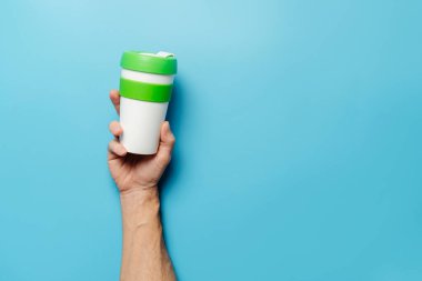 Ekoloji ve geri dönüşüm kavramı. Bir adamın eli mavi arka planda yeniden kullanılabilir plastik bir cam tutuyor..