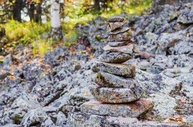 Güneşli bir günde, bir sonbahar ormanının arka planına karşı dağ yamacındaki taşlar piramidi.
