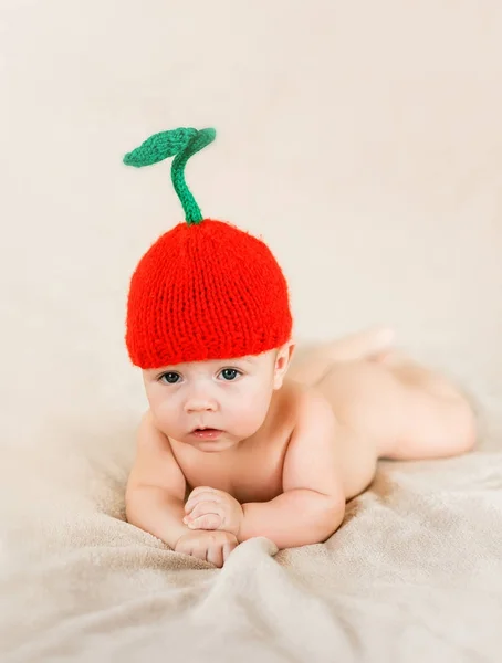 Liten bebis ligger på filten i en stickad röd körsbärshatt — Stockfoto