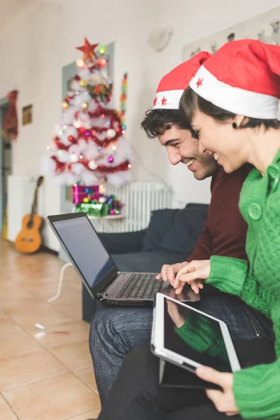 Echtpaar met santa claus hoeden met behulp van computer — Stockfoto