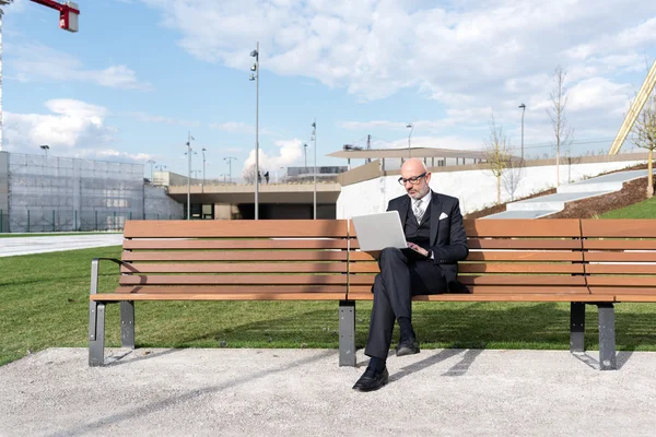Businessman on bench in city using laptop — Stock Photo, Image