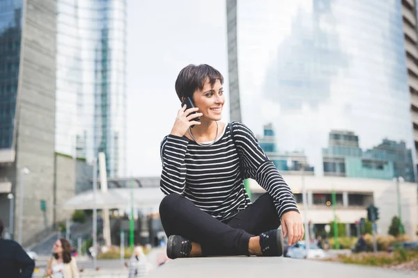 Mulher sentada na parede pequena falando smartphone — Fotografia de Stock