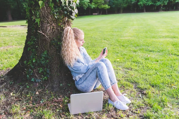 Kvinna på gräs med smartphone och bärbara — Stockfoto