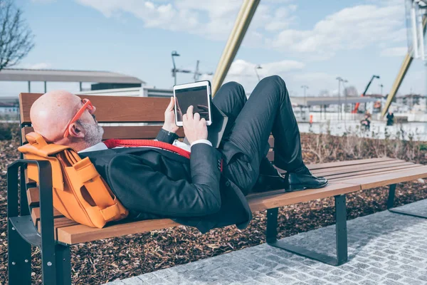 Businessman lying on bench using tablet — Stock Photo, Image