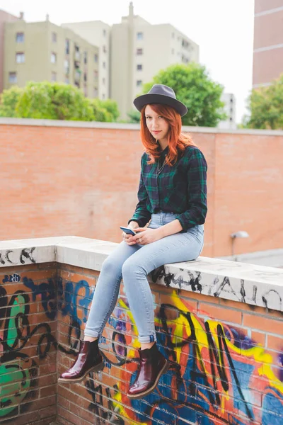 Frau sitzt auf kleiner Mauer und hält Smartphone in der Hand — Stockfoto