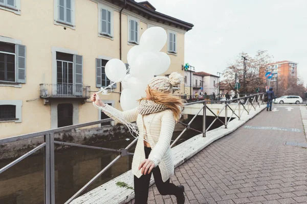 Mujer en ciudad sosteniendo globos blancos — Foto de Stock