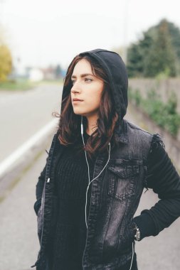 Şehirde poz veren genç, güzel bir doğu kadını kulaklıkla müzik dinliyor. Müzik, teknoloji, rahatlatıcı konsept.