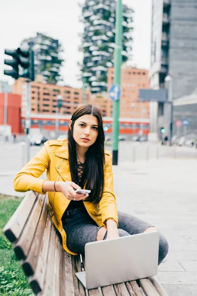 Mujer en el banco usando portátil y teléfono inteligente —  Fotos de Stock