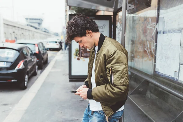 man at bus stop using smartphone