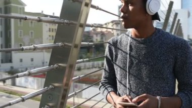 Genç yakışıklı Amerikalı Afrikalı adam arka ışık şehirde kulaklık ve akıllı telefon ile müzik dinliyor