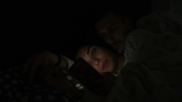 Jovem Lindo Casal Deitado Cama Abraçando Usando Telefone Inteligente Iluminado — Vídeo de Stock