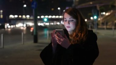 Beyaz saçlı, güzel bir kadının portresi. Akşamları açık havada telefonla konuşan, gülümseyen, aydınlanmış bir ekran ışığı - sosyal ağ, teknoloji, iletişim konsepti.