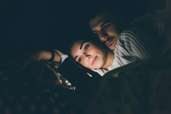 Couple using smartphone lying in bed — Stock Photo, Image
