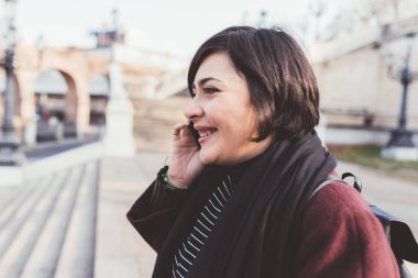 Dışarıda yürüyen genç bir kadın akıllı telefondan konuşuyor gülümsüyor - sohbet, iletişim, mutluluk konsepti
