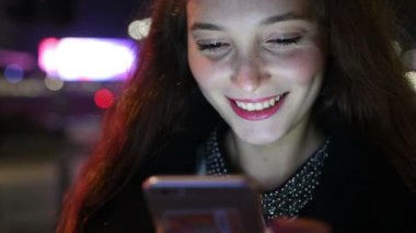 Beyaz saçlı, güzel bir kadının portresi. Akşamları açık havada telefonla konuşan, gülümseyen, aydınlanmış bir ekran ışığı - sosyal ağ, teknoloji, iletişim konsepti.
