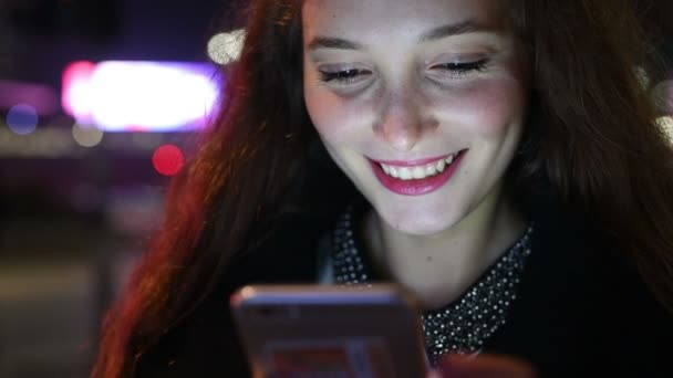 スマートフォンの手を使用して若い美しい白人の長い茶色の髪の女性の肖像画は 街の夜に屋外を保持します 顔の照明付きスクリーンライト ソーシャルネットワーク 通信コンセプト — ストック動画