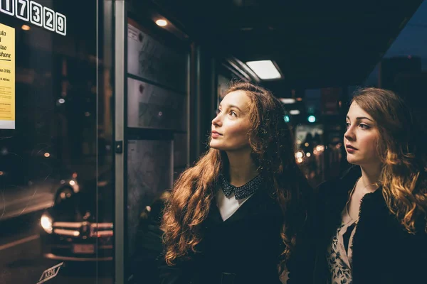 两个年轻的女性朋友站在巴士站的室外检查时刻表 公共交通的概念 — 图库照片