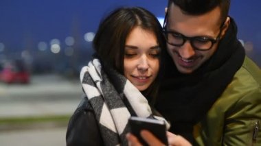 Genç ve güzel bir çift açık şehir gecesi smnart telefon teknolojisi, sosyal ağ, birliktelik konseptini kullanarak sarılıyorlar.