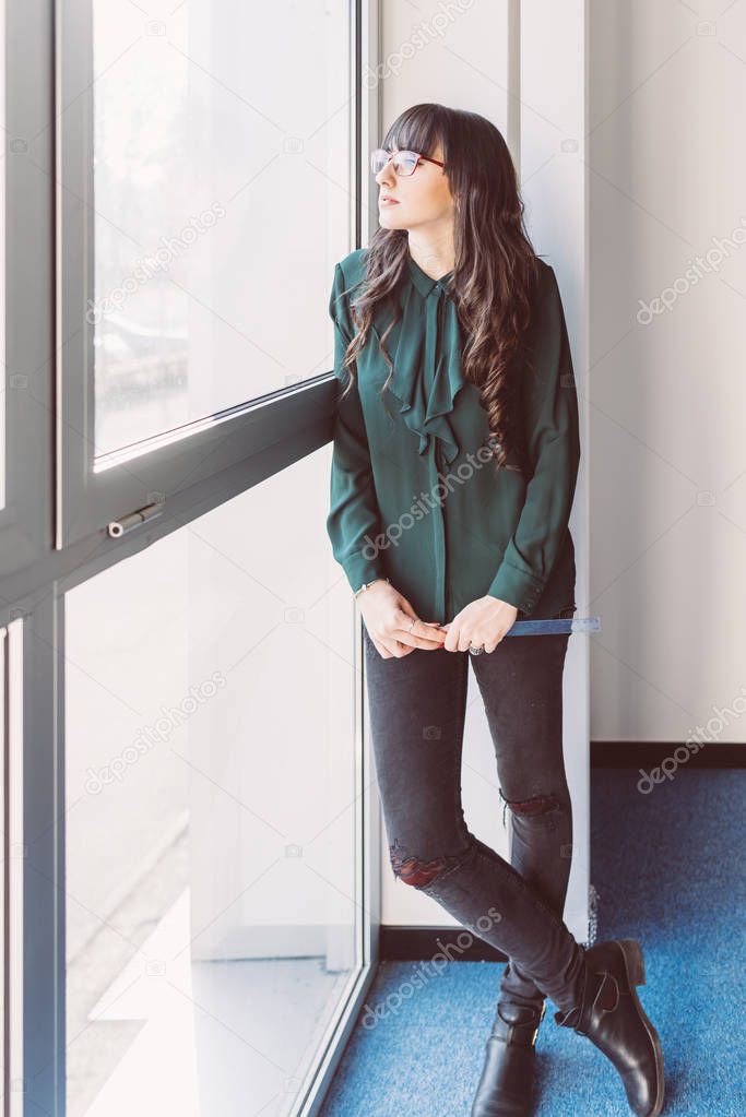 Young businesswoman looking standing near window looking outside - thinking, worried, inspiration concept 