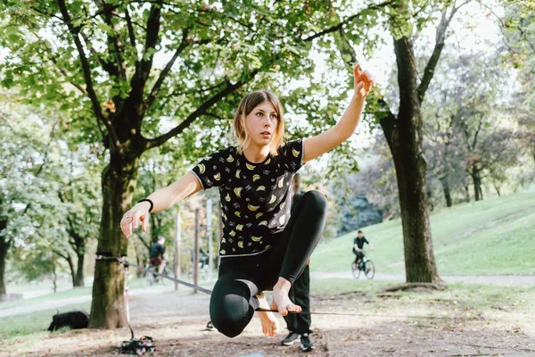 Woman balancing a tightrope or slackline outdoor in a city park in autumn