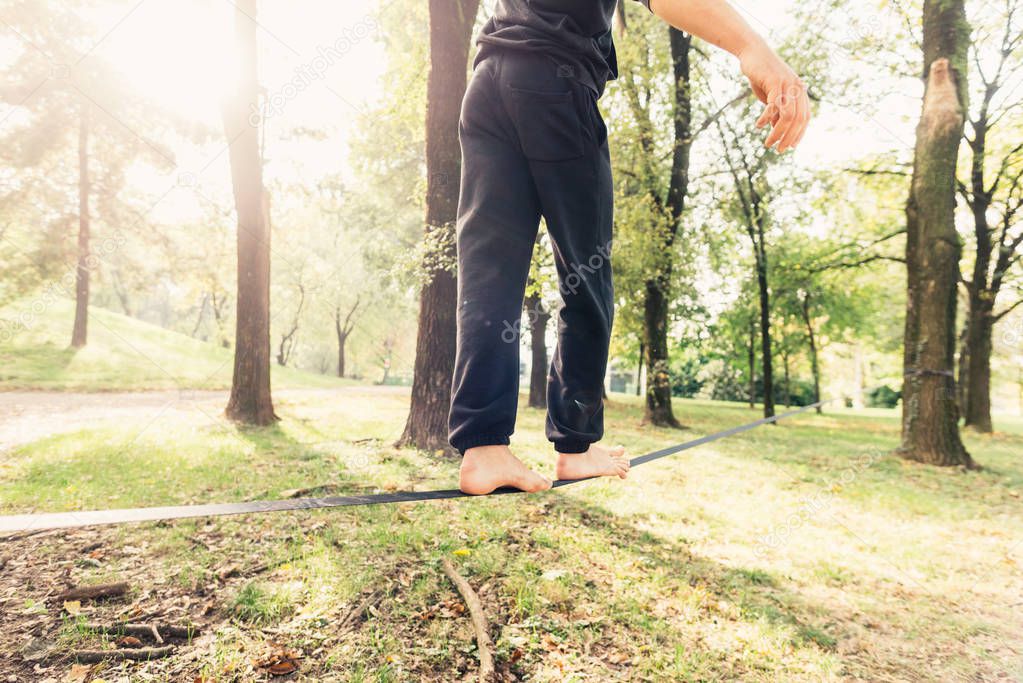 Man balancing a tightrope or slackline outdoor in a city park in autumn - slacklining, balance, training concept
