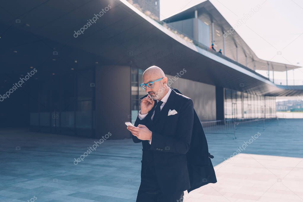 Middle-age contemporary businessman outdoor in the city, using smart phone 