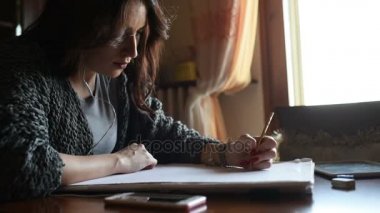 Genç, güzel, doğu doğulu bir kadın masa başında oturmuş müzik dinliyor, ders çalışıyor.