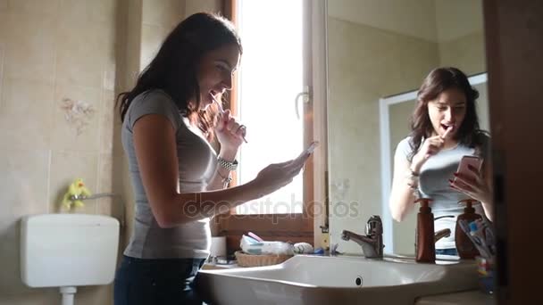 年轻漂亮的女人在浴室里一边刷牙一边讲智能手机 牙刷概念 — 图库视频影像