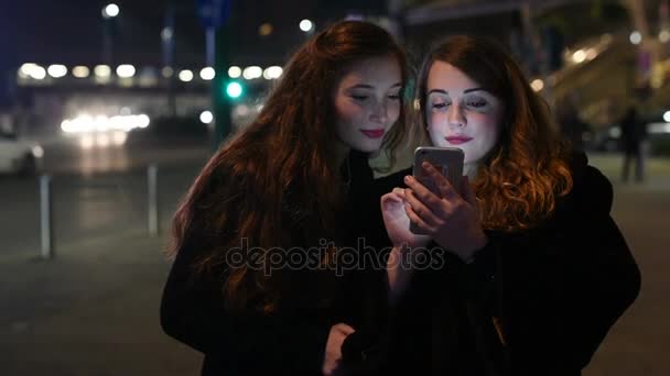 2人の若い女性がスマートフォンを使って屋外都市の夜 インターネット ソーシャルネットワーク 技術コンセプト — ストック動画