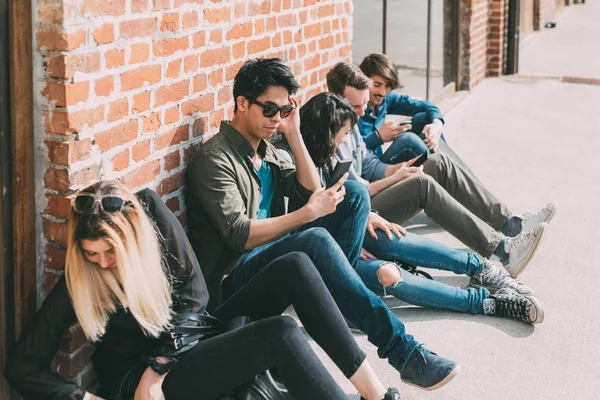 一群朋友 Multiethncit 坐在户外使用智能手机 — 图库照片