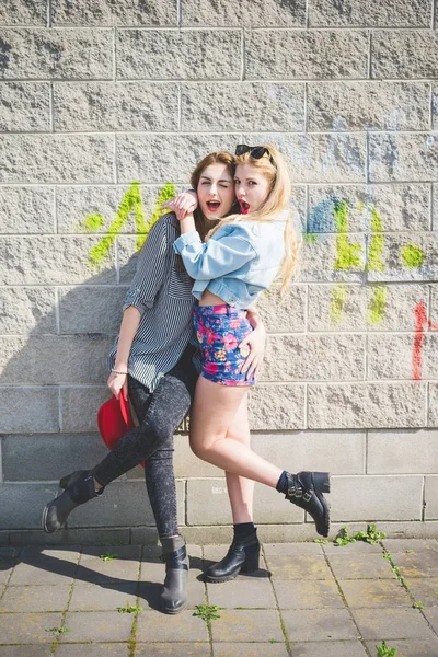 つの美しい金髪とブルネットの女の子が楽しんで市郊外の壁でポーズ — ストック写真