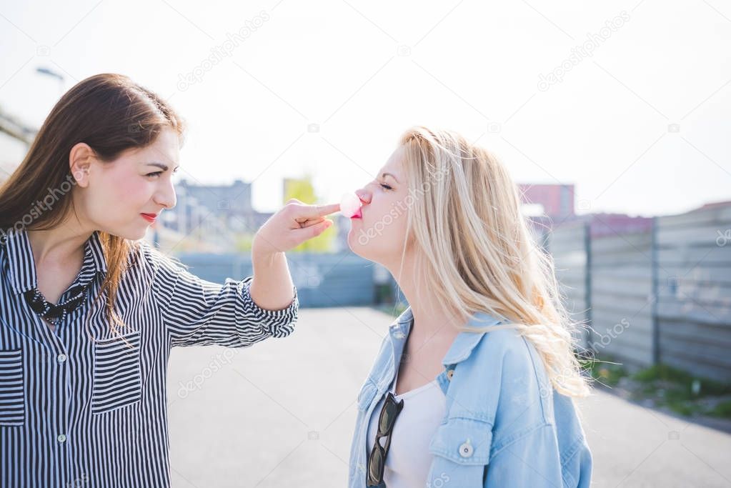 Two beautiful young women playing with bubble gum outdoor in the city