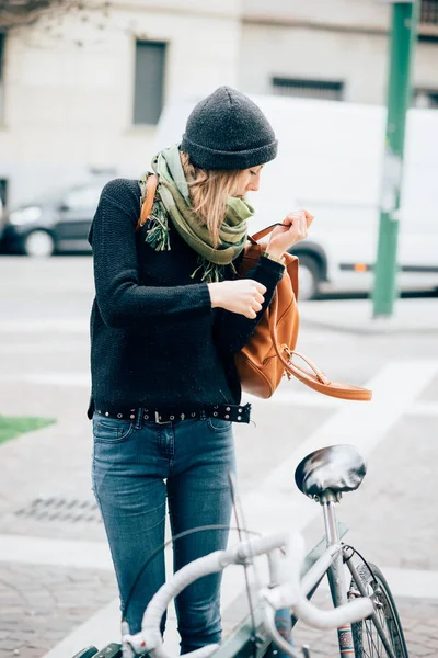 自転車の近くに立っている若い美しい女性と彼女のバックパックを取る彼女の街で離れて見て — ストック写真