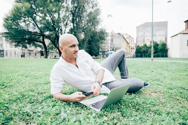 コンピューターを使用して都市公園における屋外横たわって若い現代ビジネスマン リモート作業 — ストック写真