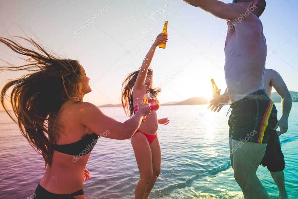 Group of friends millennials having fun on the beach, drinking beer
