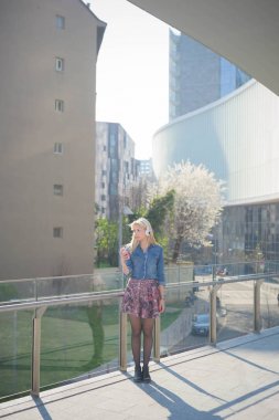 Genç güzel beyaz sarışın kız gülümseyerek kulaklık ile şehrin smartphone ile müzik dinlemek