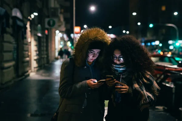 Två Unga Kvinnor Multietnisk Utomhus Med Hjälp Smarttelefon Utomhus Natten — Stockfoto