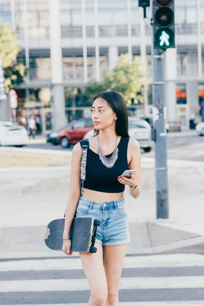 Açık Yürüyen Genç Kadın Kaykay Tutan Smartphone Kullanarak — Stok fotoğraf