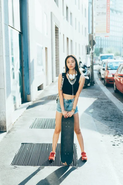 Joven Mujer Posando Aire Libre Sosteniendo Monopatín Escuchando Música —  Fotos de Stock