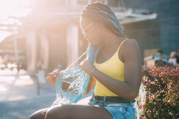 Joven hermosa mujer negra sititng solo al aire libre retroiluminación plumas —  Fotos de Stock
