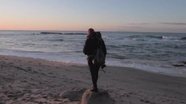 Woman on seashore looking horizon at sunset