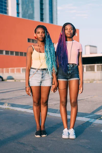 Dos hermosas hermanas negras jóvenes cogidas de la mano escuchando música — Foto de Stock