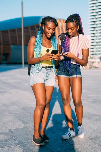 Две молодые красивые черные сестры на открытом воздухе с помощью смартфона — стоковое фото