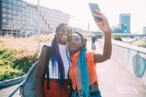 Genç, güzel siyah kız kardeşler arka planda akıllı telefon kullanıyorlar. — Stok fotoğraf