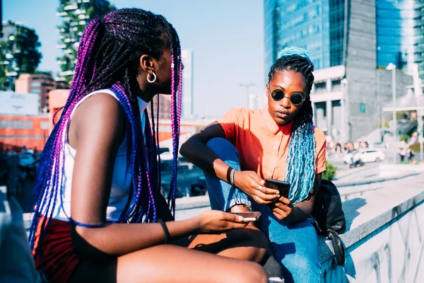 Две сестры сидят на улице, разговаривают и пользуются смартфоном — стоковое фото