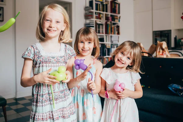 Three little sisters indoor at home playing with balloon looking — 스톡 사진