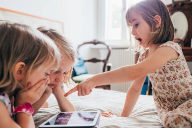 Evde yatağında tablet kullanan üç kız kardeş.
